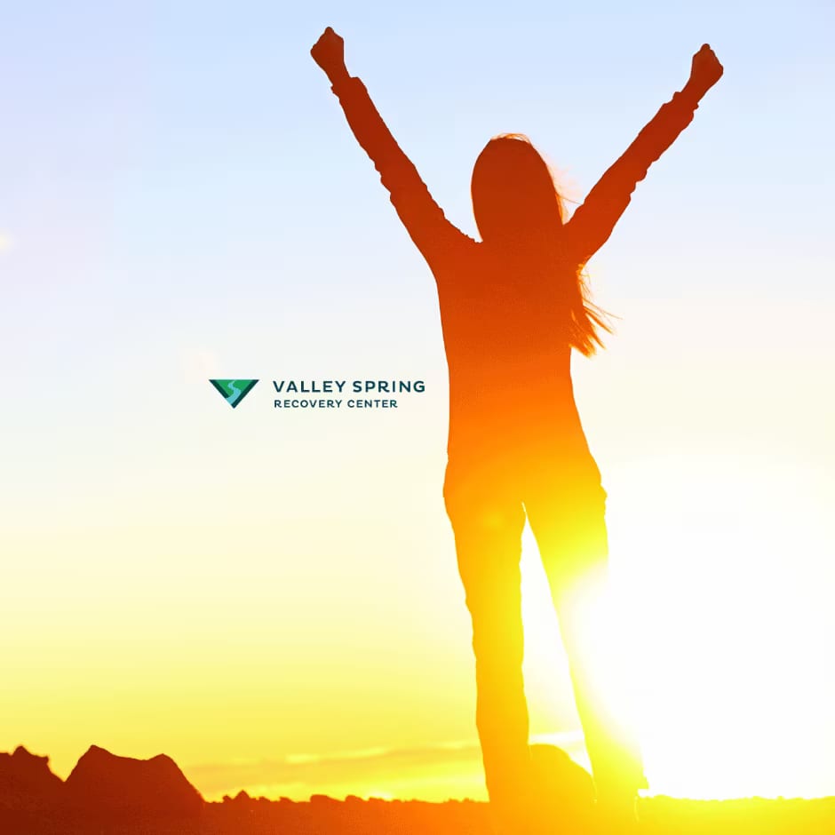 Recovery after sedative addiction treatment Person raising both arms at sunrise beside the Valley Spring Recovery Center logo, representing recovery after sedative addiction treatment