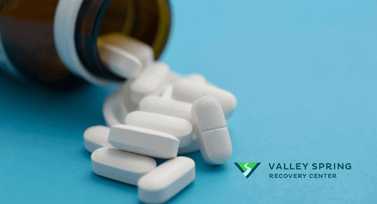 Prescription tablets on a blue surface beside the Valley Spring Recovery Center logo