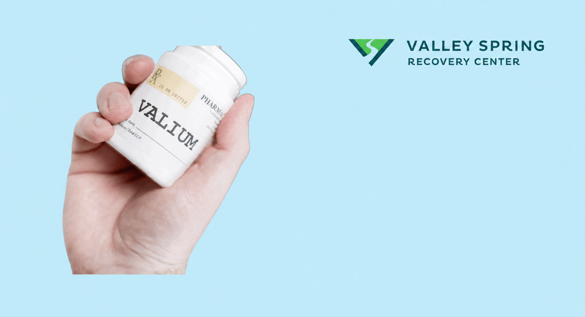 Hand holding a Valium medication container in a branded Valley Spring Recovery Center article graphic