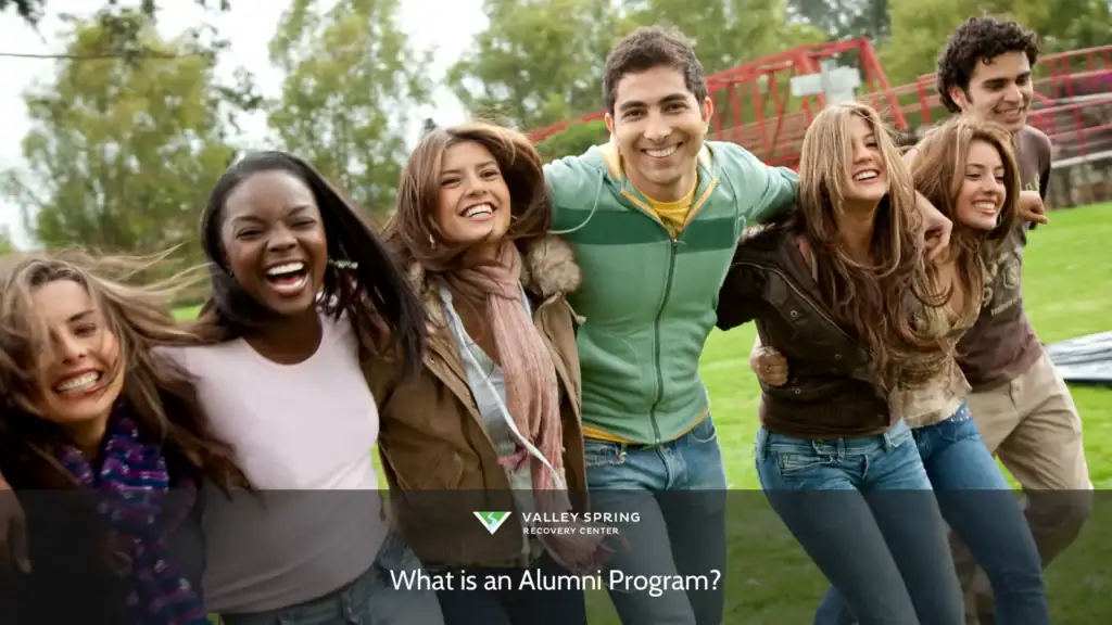 A diverse group of young adults joyfully linking arms and laughing together outdoors, capturing the essence of camaraderie in an alumni program setting.