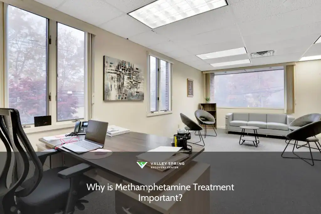 Bright therapy office featuring a modern desk setup, comfortable seating, and large windows showcasing autumn foliage, emphasizing a welcoming atmosphere.