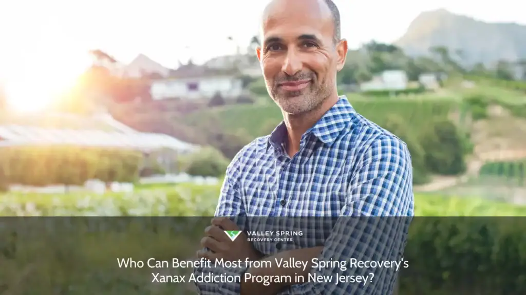 Smiling man in a checked shirt stands confidently in a vineyard at sunset, representing community wellness and recovery programs in New Jersey.