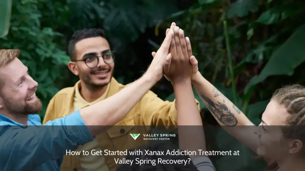 Hands joining in a high-five among a diverse group, symbolizing collaboration and support, set against a lush green backdrop at Valley Spring Recovery.